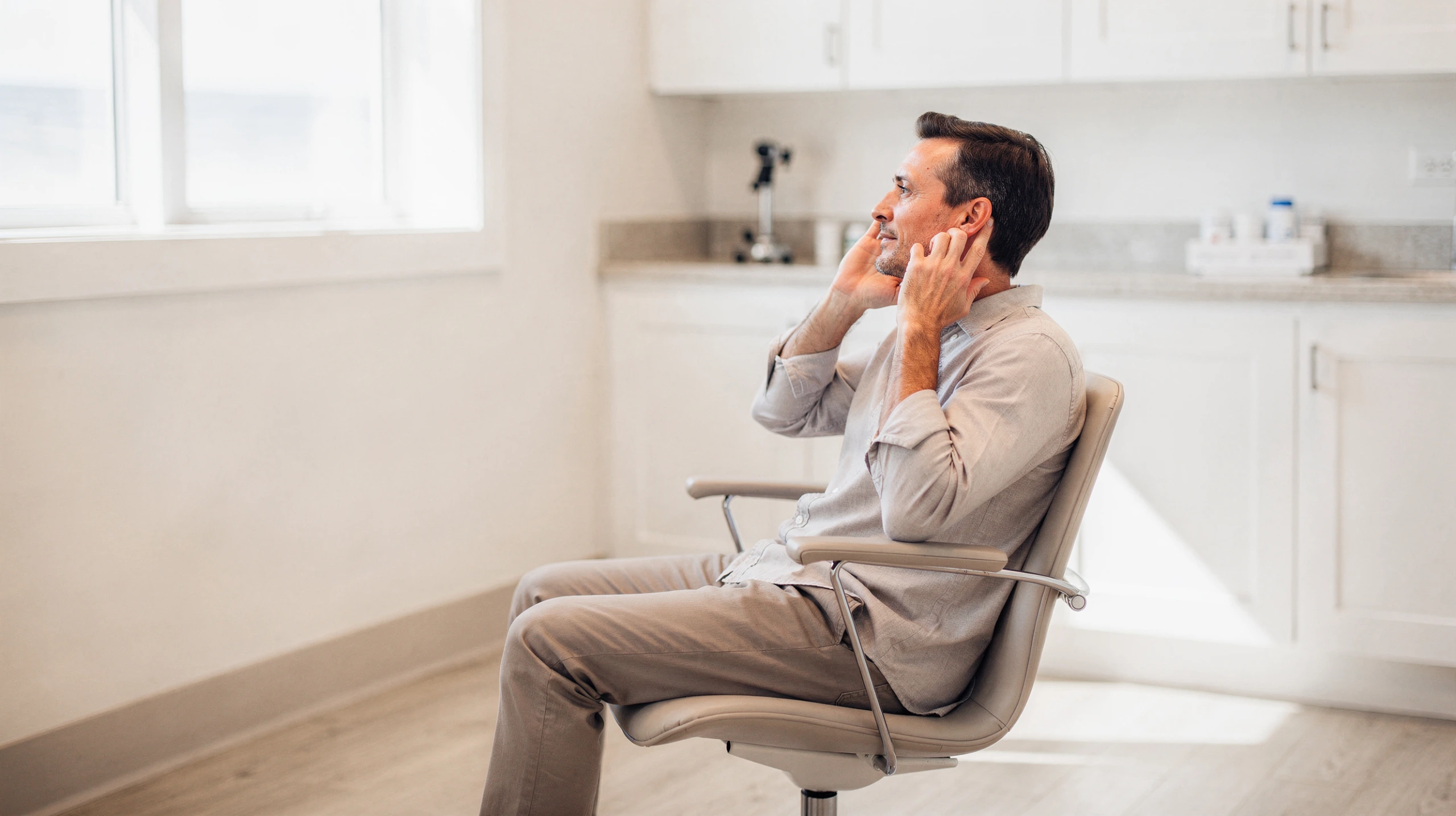 Man sitting in a clinic exam chair, holding his face with both hands in discomfort